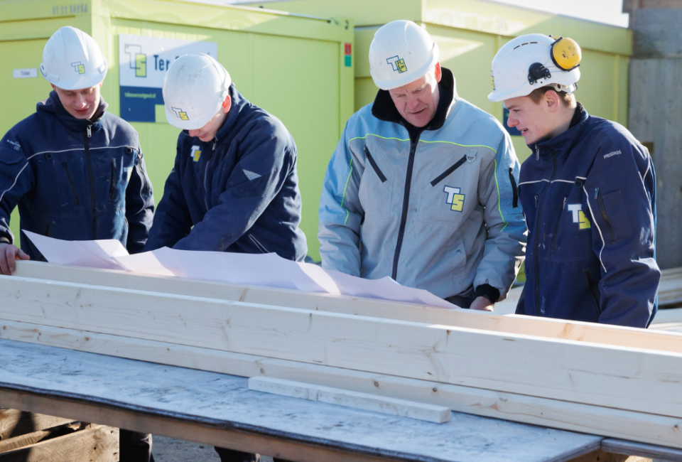 Uitvoerder en studenten kijkend naar tekeningen op de bouwplaats